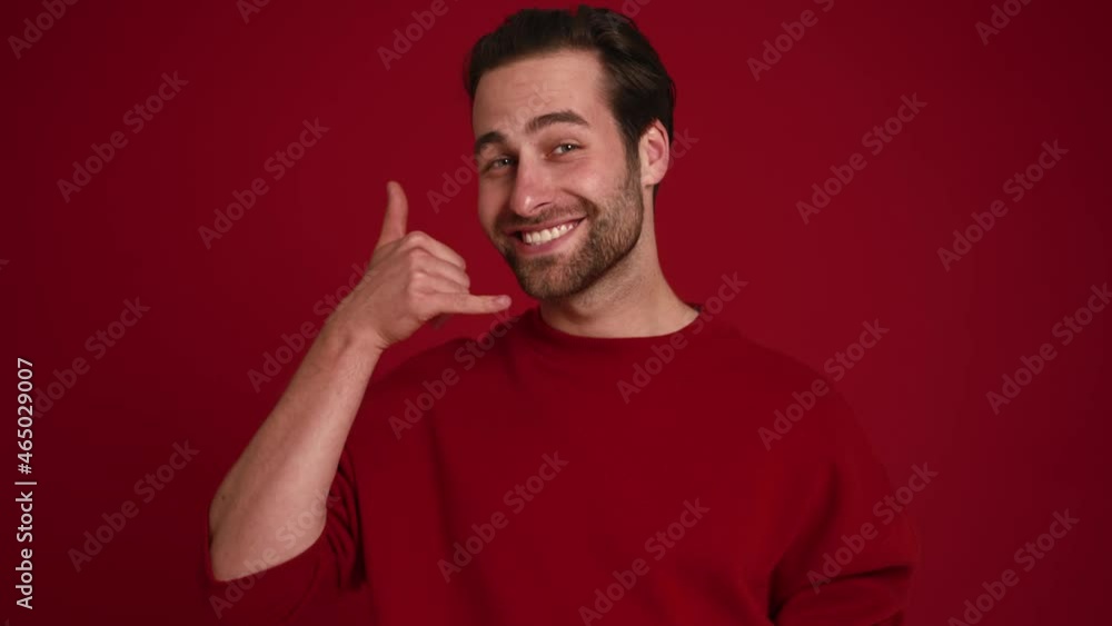 Smiling man showing call me gesture in red studio Smiling man showing call me gesture in red studio