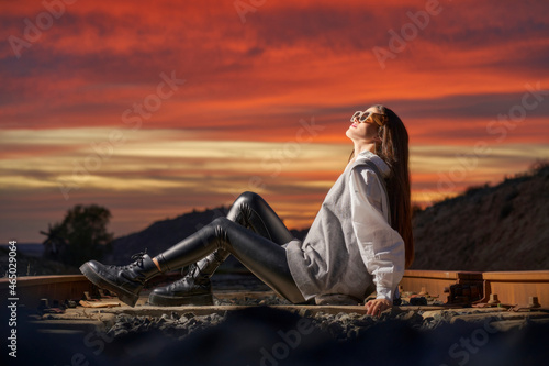 A teenage girl sitting on the railroad tracks in the evening light.