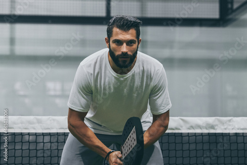 Beautiful man playing paddle tennis, racket in hand   concentrated look. Young sporty boy ready for the match. Focused padel athlete ready to receive the ball. Sport, health, youth and leisure concept photo