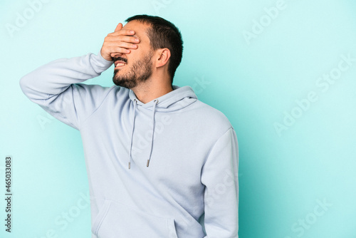 Young caucasian man isolated on blue background covers eyes with hands, smiles broadly waiting for a surprise.