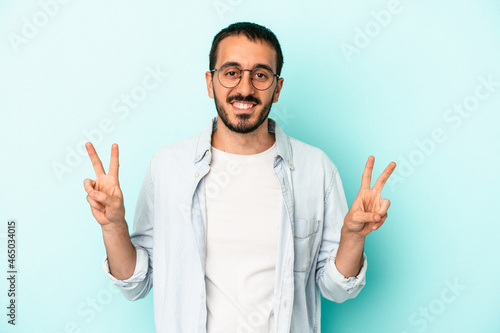 Young caucasian man isolated on blue background showing victory sign and smiling broadly.