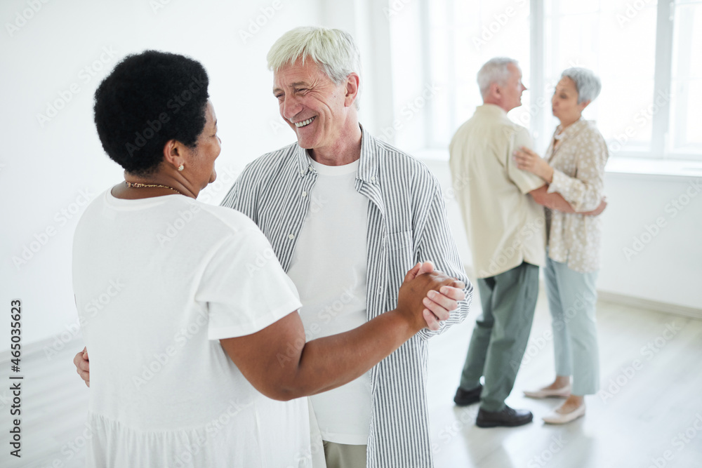 Two senior couples smiling to each other holding hands while dancing a slow dance in dance studio Two senior couples smiling to each other holding hands while dancing a slow dance in dance studio