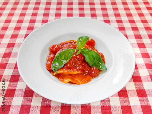 Ravioli pasta plate with fresh tomato sauce and basil on squared tablecloth