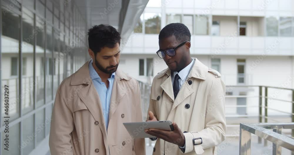 Multiethnic business partners with tablet standing outside and talking Multiethnic business partners with tablet standing outside and talking