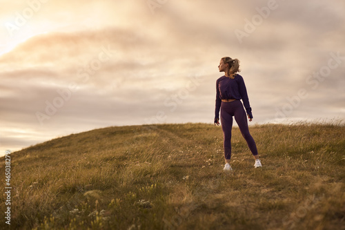 Sportswoman standing on hill in sunset