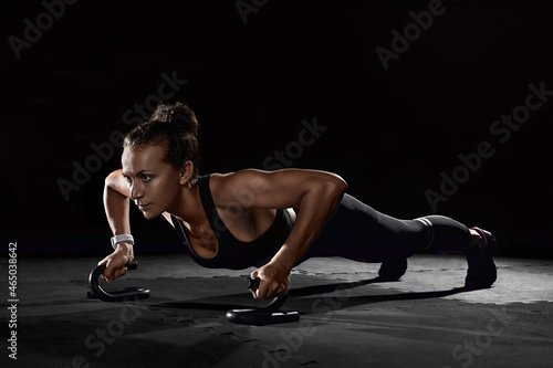 Female athletes with holders doing push-ups in gym in darkness