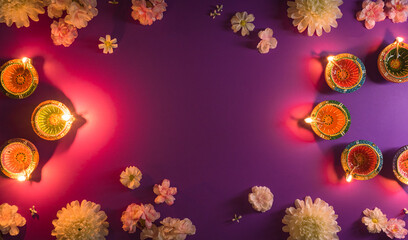 Happy Diwali - Clay Diya lamps lit during Dipavali, Hindu festival of lights celebration. Colorful traditional oil lamp diya and flowers on purple background