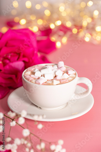 Cup of cocoa with marshmallows, pink rose and white flowers on a pink background, vertical photo