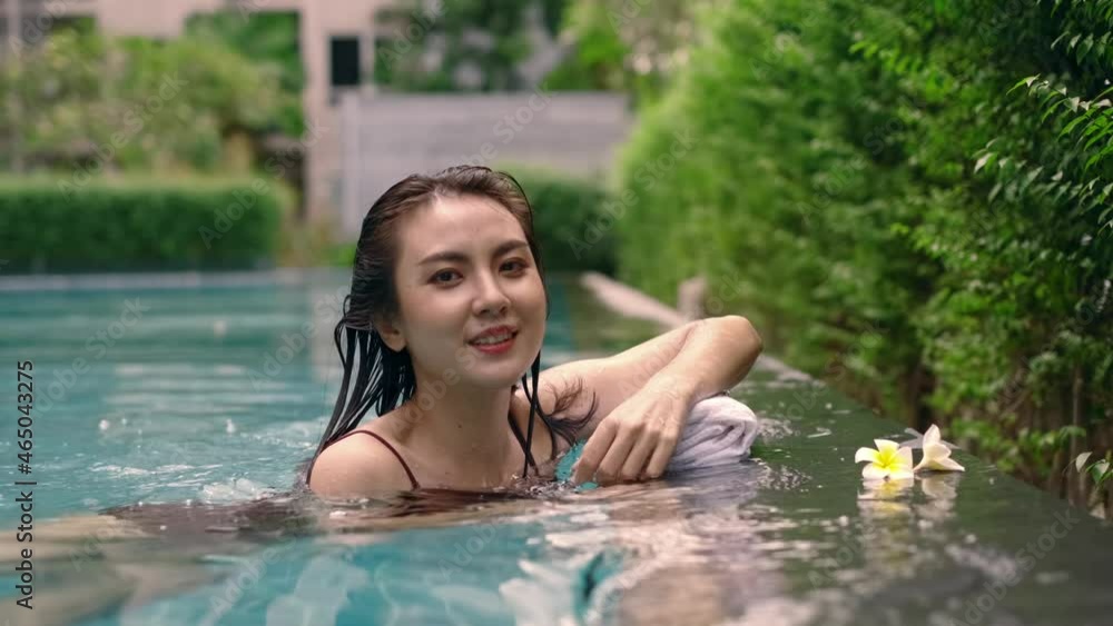 4K Slow motion. Beautiful attractive Asian woman resting and swimming in resort pool with nature. Young female in swimsuit relaxation on pool in summer. Vacation time relaxing by tropical pool. 4K Slow motion. Beautiful attractive Asian woman resting and swimming in resort pool with nature. Young female in swimsuit relaxation on pool in summer. Vacation time relaxing by tropical pool.