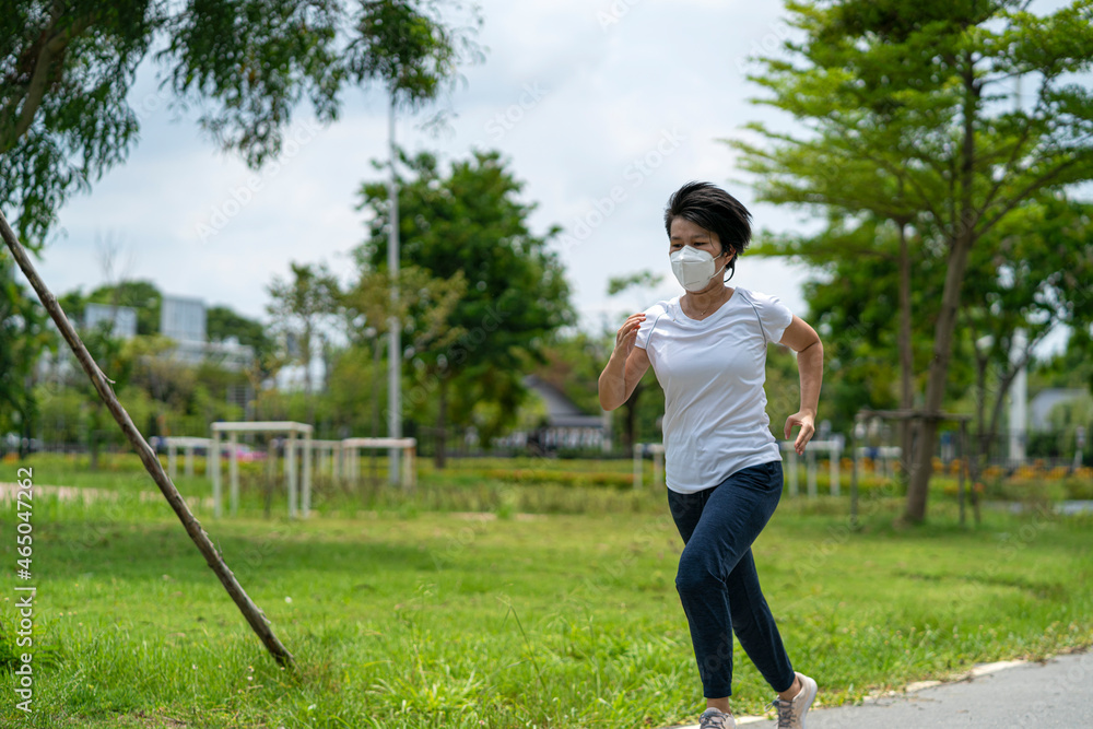 Asian woman wearing face mask while she running in public park after coronavirus outbreak and city lockdown a new normal life. social distancing, new normal, covid-19 or running concepts