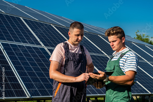 against the background of solar panels, two workers write in a tablet plan of work performed