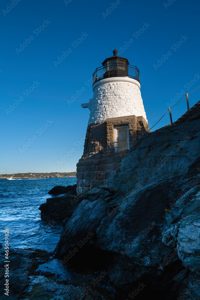 White lighthouse on the rocky cliff over the blue ocean water against clear sky. Castle Hill Lighthouse in Newport, Rhode Island.
