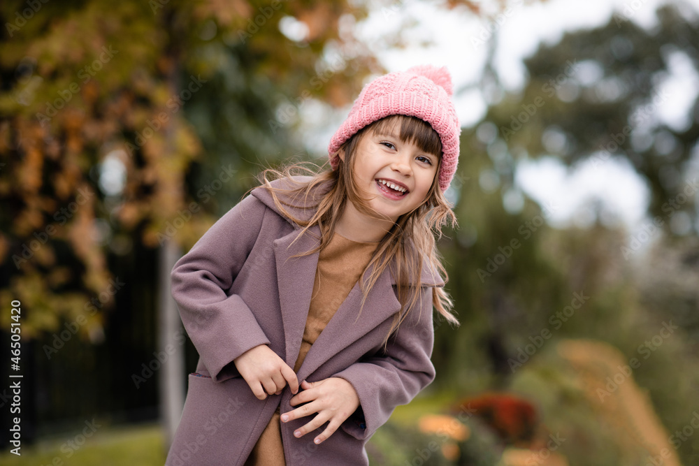 Happy cute child girl 4-5 year old wear knit wool hat and jacket over nature backggound outdoors. Autumn season. Looking at camera. Happiness. Laughing little kid having fun in park. Childhood. Happy cute child girl 4-5 year old wear knit wool hat and jacket over nature backggound outdoors. Autumn season. Looking at camera. Happiness. Laughing little kid having fun in park. Childhood.