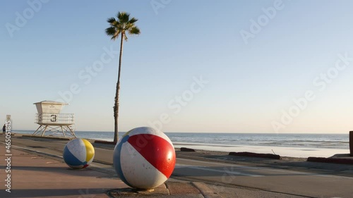 Pacific ocean beach, Oceanside California USA. Ball, lifeguard tower, life guard watchtower hut and tropical palm tree, sky, beachfront street, waterfront road. Los Angeles vibes, aesthetic atmosphere
