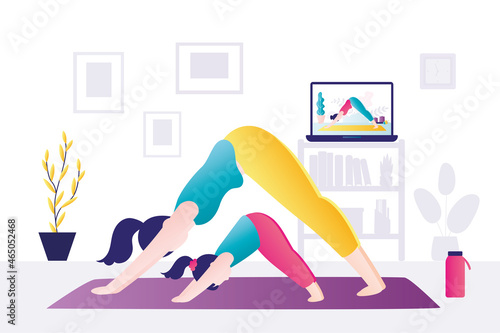 Mom and daughter stand in yoga pose, downward - facing dog. Woman and kid practice yoga together. Remote sports activities. Family leads healthy lifestyle. Online course on laptop.