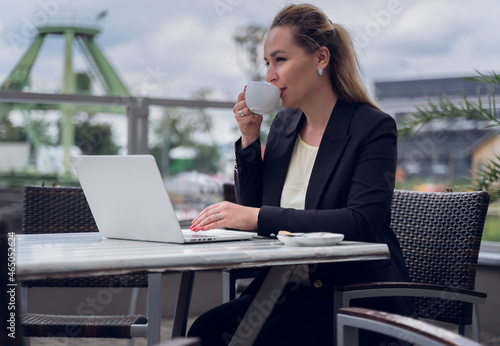 Businesswoman woman sits drinking coffee while working on a laptop on a terrace