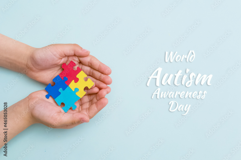 World autism awareness day. The hands of a small child close up holding colorful puzzles on blue background. Banner
