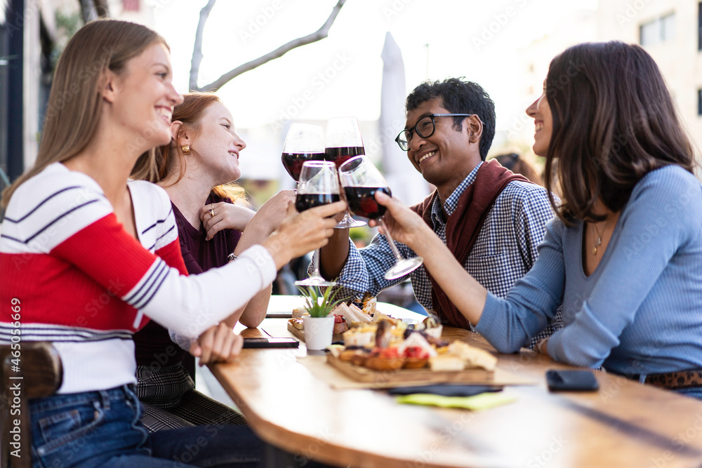 Multiracial friends toasting red wine at the outdoor pub - Food and beverage lifestyle concept with happy people having fun together at pub - Bright filter with focus on the guys in the background