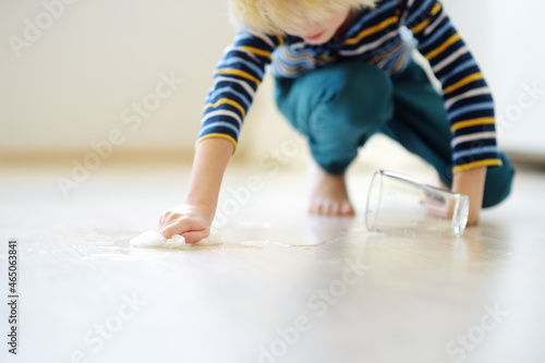Fotografie Little boy wipes water spilled from a glass on the floor