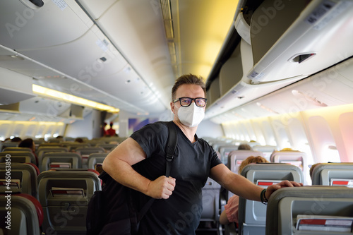 Handsome mature man in protection face mask during boarding in airplane. Safety transportation while coronavirus epidemic.