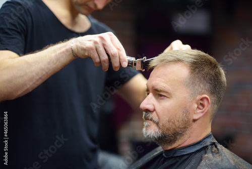 Hairdresser is cutting hair of handsome bearded mature man in salon. Stylist making hairstyle for person in barbershop. Services of a professional stylist.
