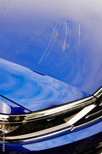 Blue car with huge scratches on hood. Vandalism or crash accident. Insurance case. Polishing and repairs needed. Vertical photo. Closeup.