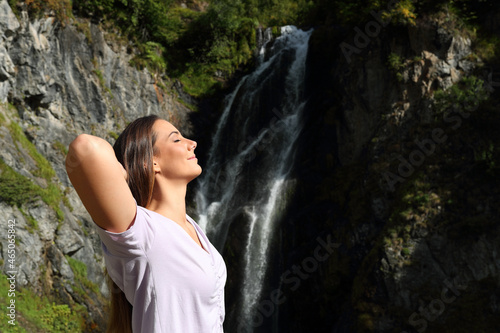 Relaxed woman breathing fresh air and resting in a waterfall