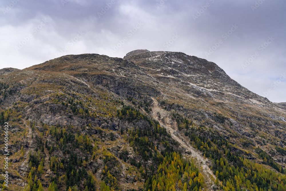 harsh mountain in the Swiss Alps with low shrubs and sparse vegetation and light snow on the peak under an ominous and overcast sky