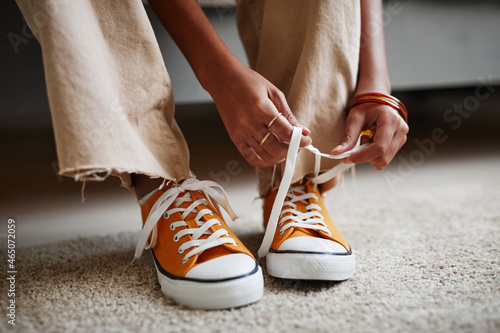Close up of unrecognizable teenage girl tying laces on bright orange sneakers, copy space