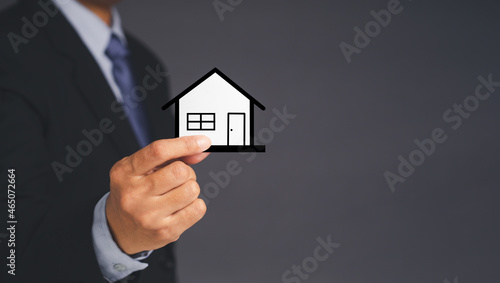 Business and real estate concept. A businessman s holding a mini paper house while standing over gray background. Space for text. Close-up photo. Property insurance and security