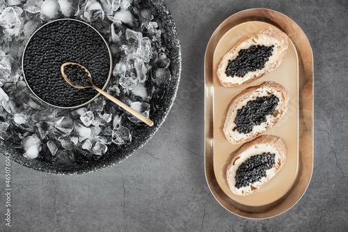 Black caviar in can on ice and bread with butter on golden plate