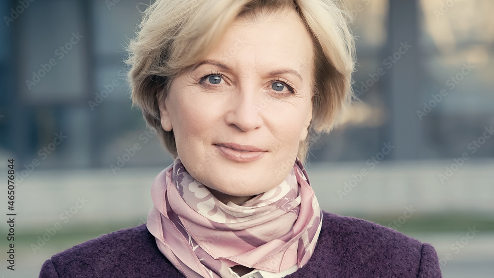 positive middle aged woman in neck scarf looking at camera outdoors. positive middle aged woman in neck scarf looking at camera outdoors.