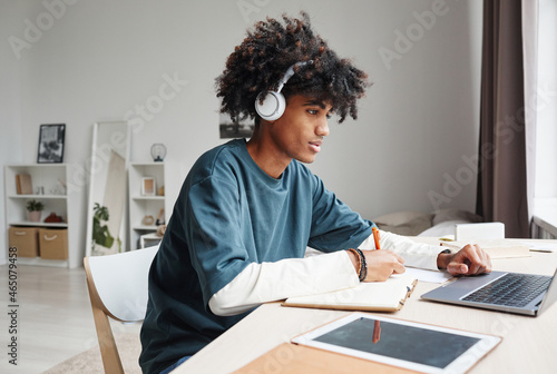 Side view portrait of African-American teenage boy studying at home or in college dorm and using laptop  copy space
