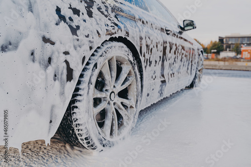 Vehicle in white soapy foam during regular car wash outdoors, auto getting wash with soap