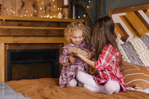 Children open a gift box. The sisters are packing a Thanksgiving present. Holiday christmas at home. Boho bedroom interior. Siblings lifestyle moments. Birthday congratulations. In plaid dresses