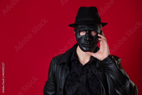 A mysterious ninja assassin in a noir style. A man in black leather clothes with a coat and hat, covers his face with a mask. Photo on red