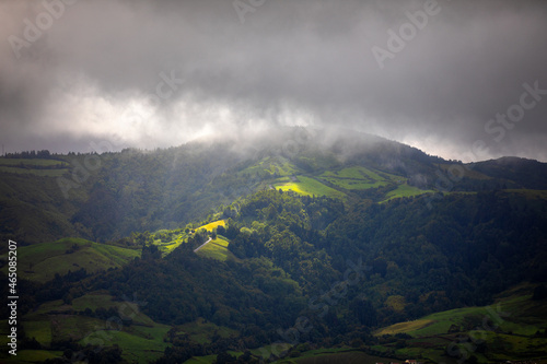 Bright sunlight shining through hole of clouds to dark scene of mountain range, Azores, Sao Miguel, Portugal. The beam of light through the dark clouds on the mountains in Azores, Portugal. © daliu
