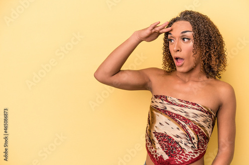 Young latin transsexual woman isolated on yellow background looking far away keeping hand on forehead. © Asier