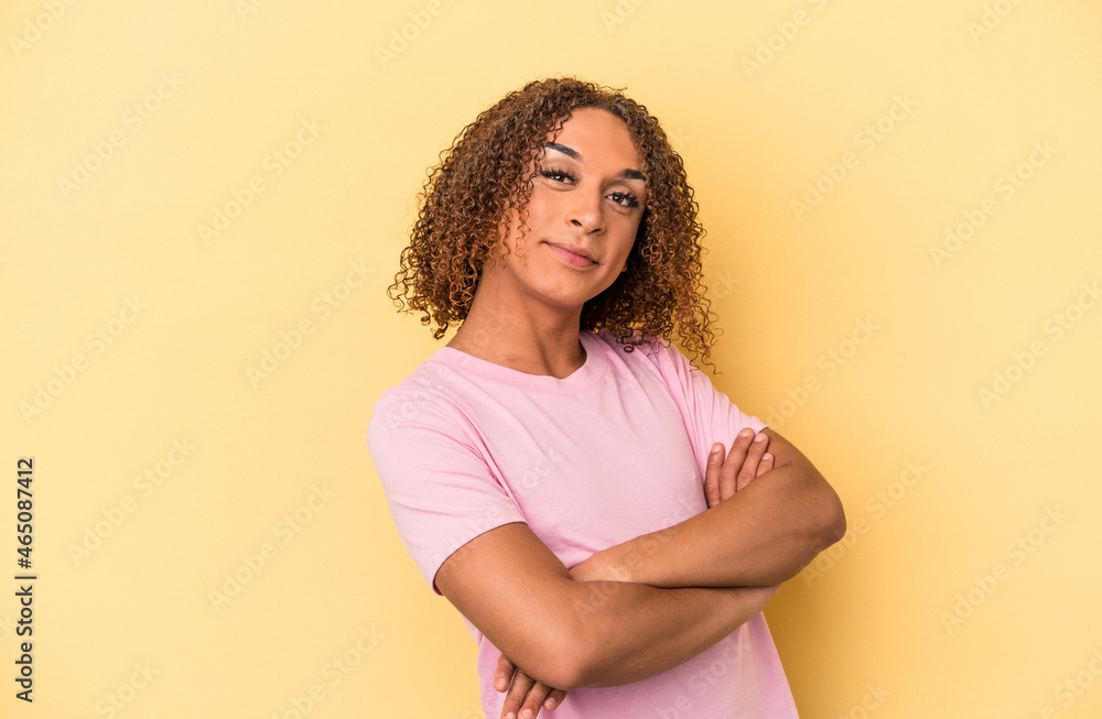 Young latin transsexual woman isolated on yellow background who feels confident, crossing arms with determination. Young latin transsexual woman isolated on yellow background who feels confident, crossing arms with determination.