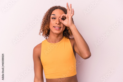 Young latin transsexual woman isolated on pink background excited keeping ok gesture on eye.