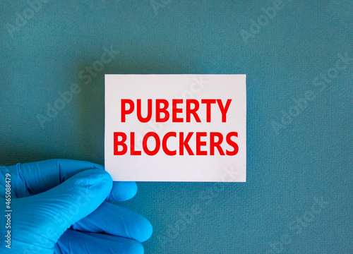 Medical and puberty blockers symbol. Words 'puberty blockers' on white card. Doctor hand in blue glove. Beautiful white background. Copy space. Medical and puberty blockers concept.