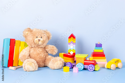 Kids toys collection. Teddy bear, wooden train, rainbow color xylophone and baby toys on light blue background. Front view