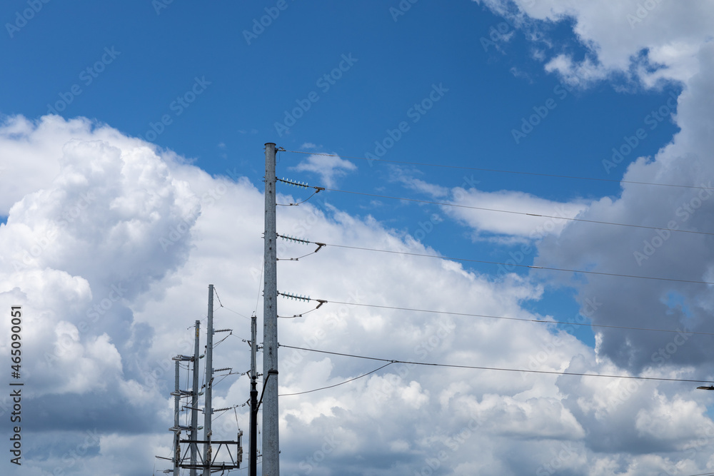 View of the tops of several metal electrical poles, each carrying multiple lines, against a blue sky with white clouds, horizontal aspect View of the tops of several metal electrical poles, each carrying multiple lines, against a blue sky with white clouds, horizontal aspect