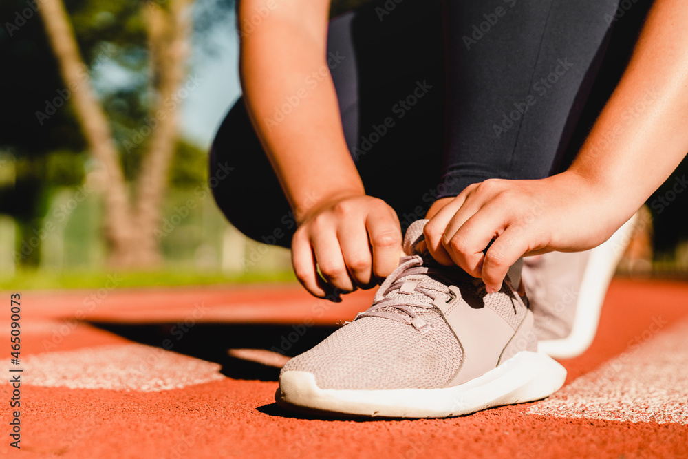 Close up cropped shot of a woman athlete tying sporty shoes, active wear, sneakers for training workout jogging running in stadium outdoors. Close up cropped shot of a woman athlete tying sporty shoes, active wear, sneakers for training workout jogging running in stadium outdoors.