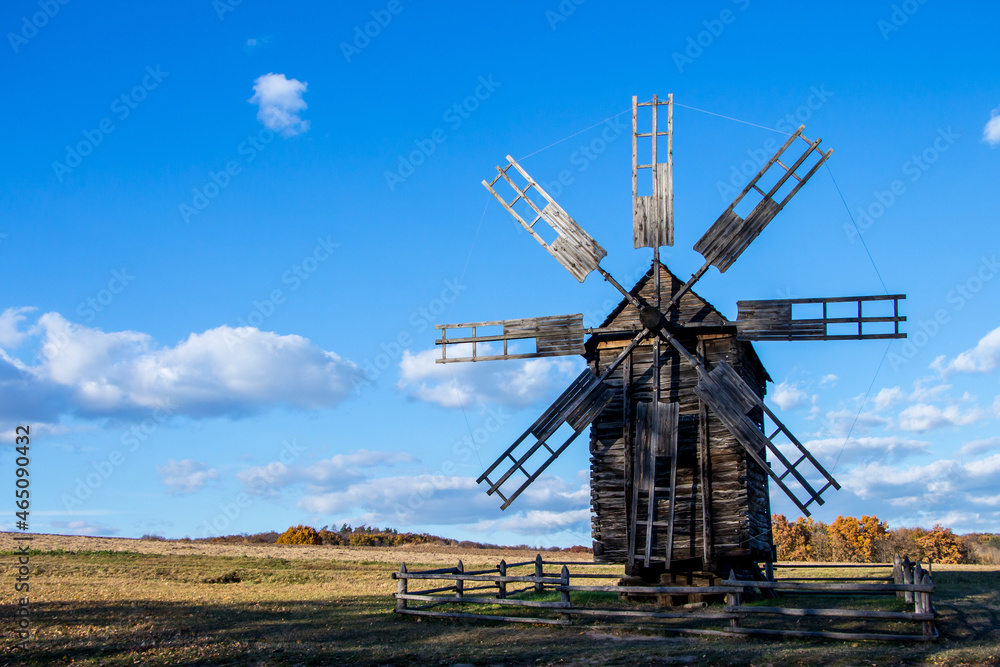 old wooden mill for grinding grain into flour, against the background of a field and a clear, blue sky with a small amount of clouds, free space