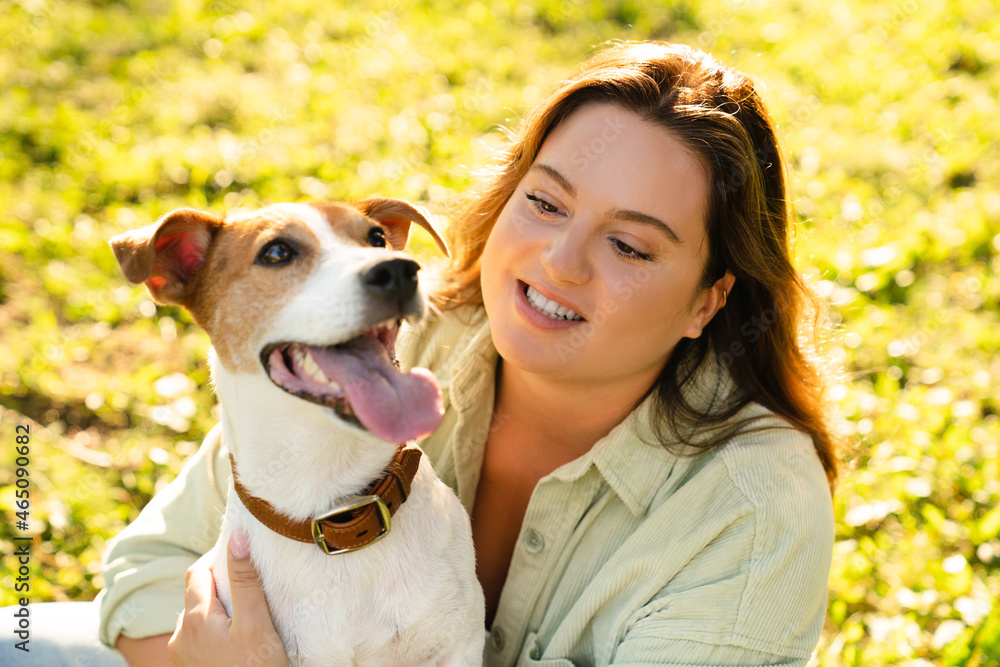 Close up photo of jack russell terrier playing walking with young pet female owner outdoors in park on green lawn. Dog care adoption concept. Close up photo of jack russell terrier playing walking with young pet female owner outdoors in park on green lawn. Dog care adoption concept.