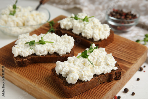Bread with cottage cheese and microgreens on white table, closeup