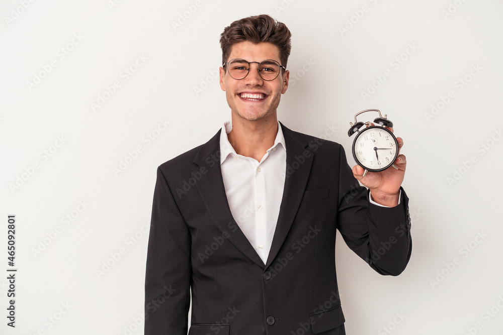 Young business caucasian man holding alarm clock isolated on white background happy, smiling and cheerful.