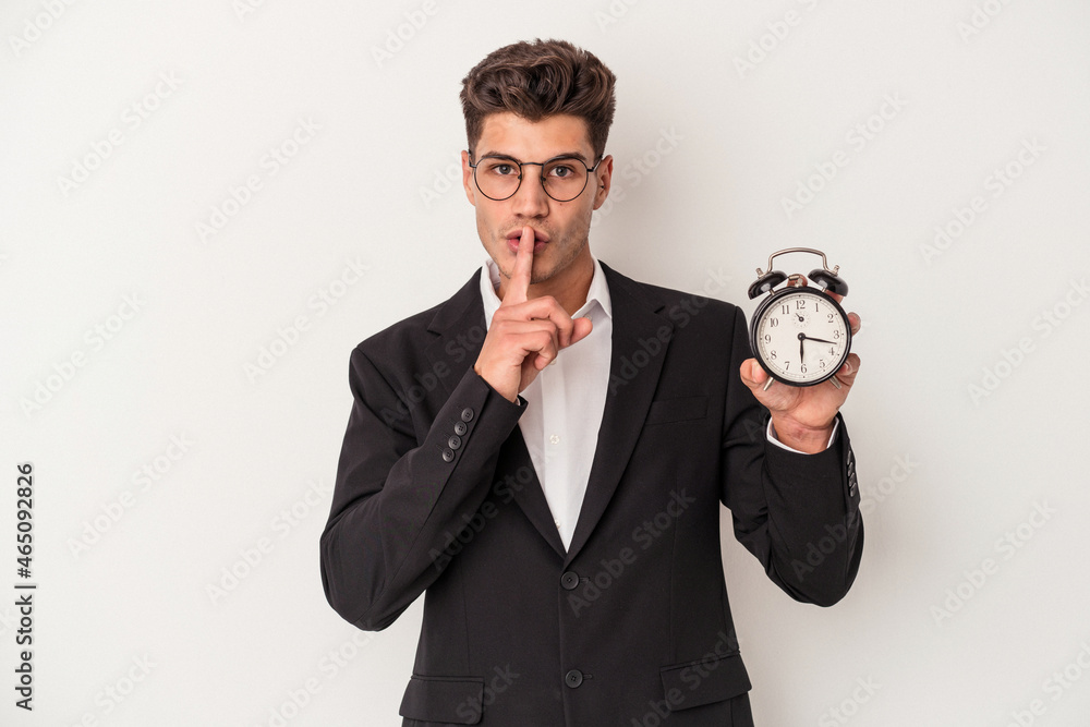 Young business caucasian man holding alarm clock isolated on white background keeping a secret or asking for silence. Young business caucasian man holding alarm clock isolated on white background keeping a secret or asking for silence.