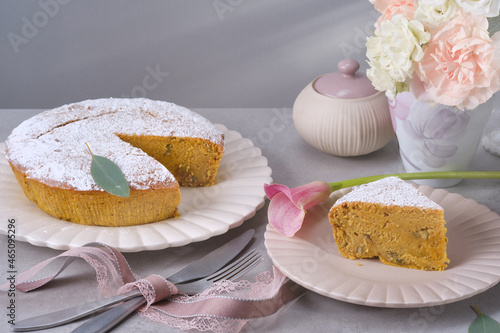 Muffin or bundt cake decorated icing sugar on the plate with knife and fork on the granite table. Christmas Stollen traditional European festive dessert against vase with white and pink flowers.  photo